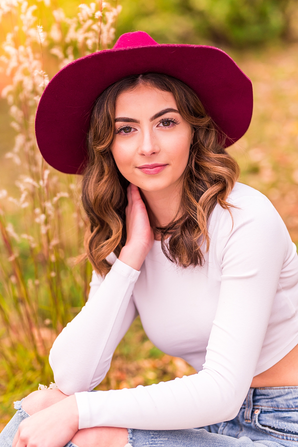 senior girl sits near tall grass in red hat