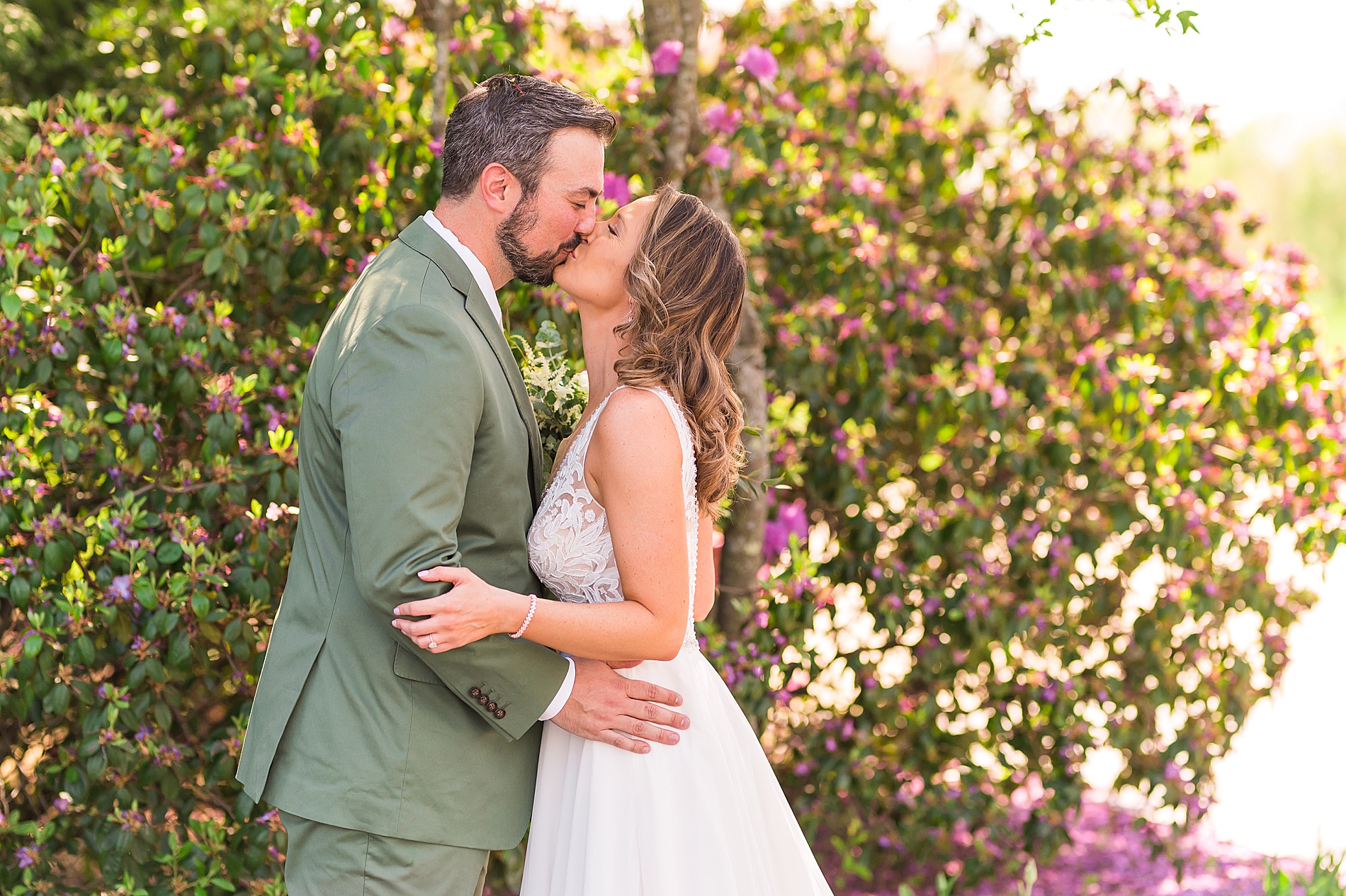 bride and groom kiss in front of blossoming bush 
