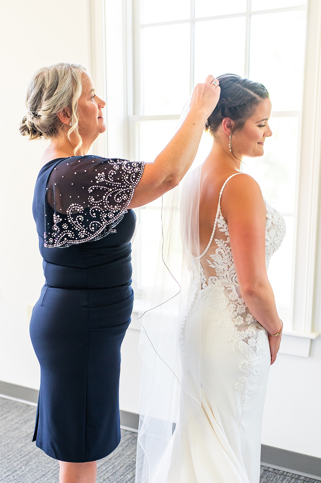 bride's mom helps her put on veil right before wedding