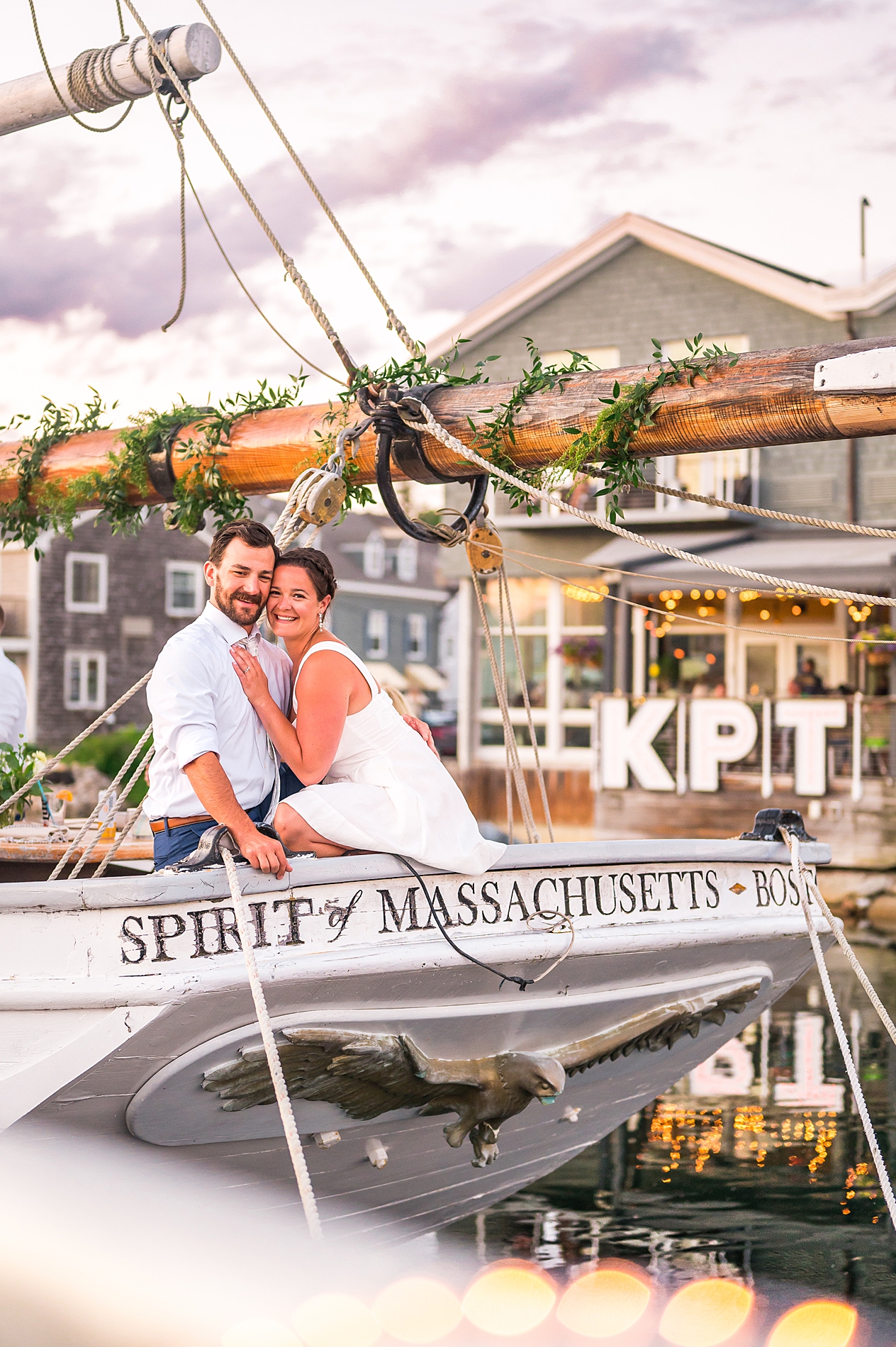 newlyweds sit on front of sailboat after Timeless Sunset Beach Wedding
