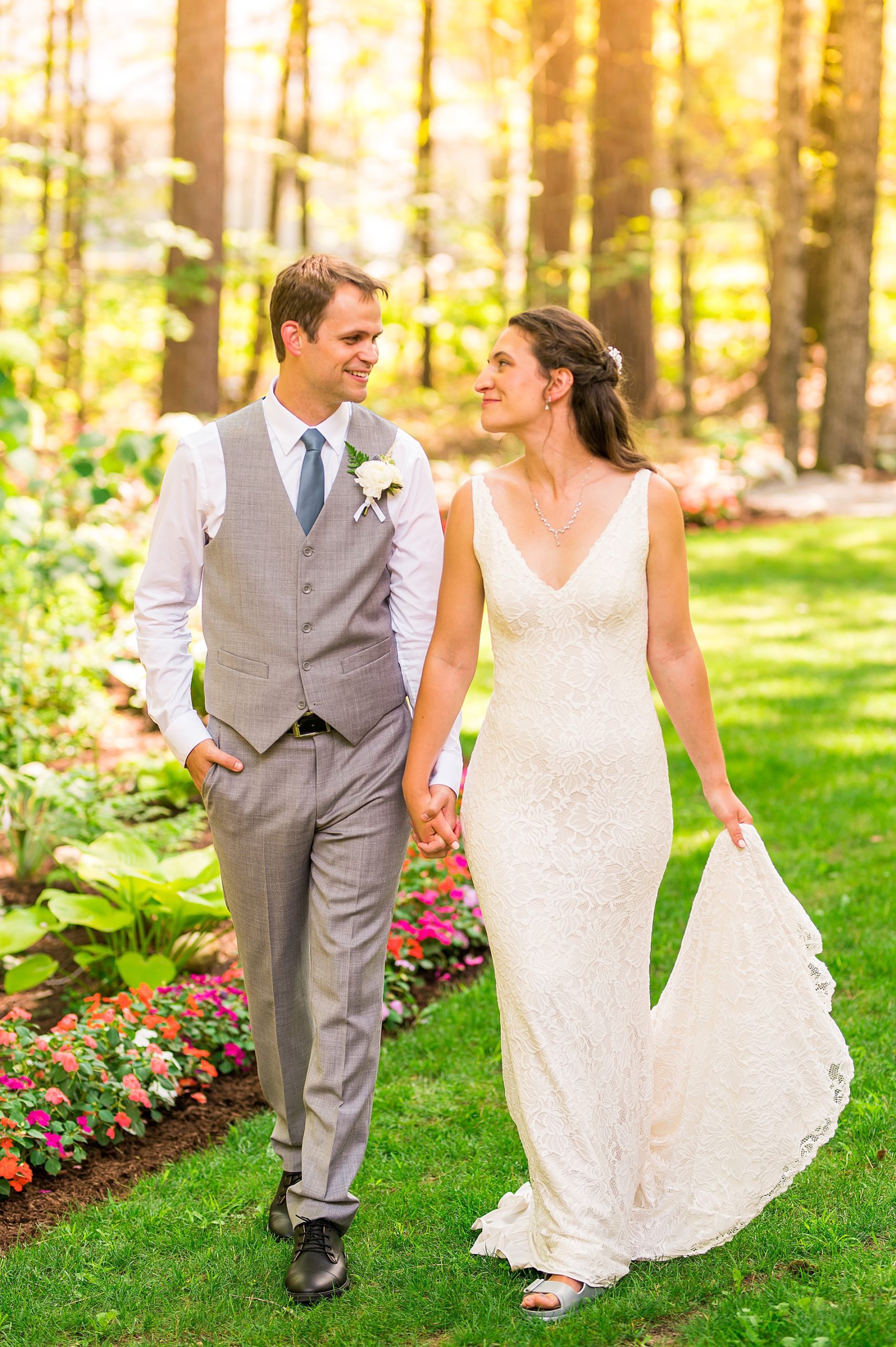 couple walking along flower lined path during first look moment 