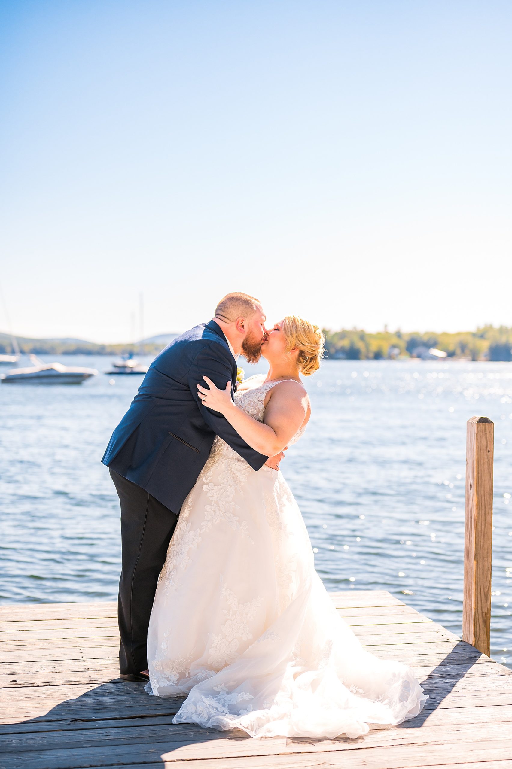 newlyweds kiss on boat dock by lake at Wolfeboro Inn 