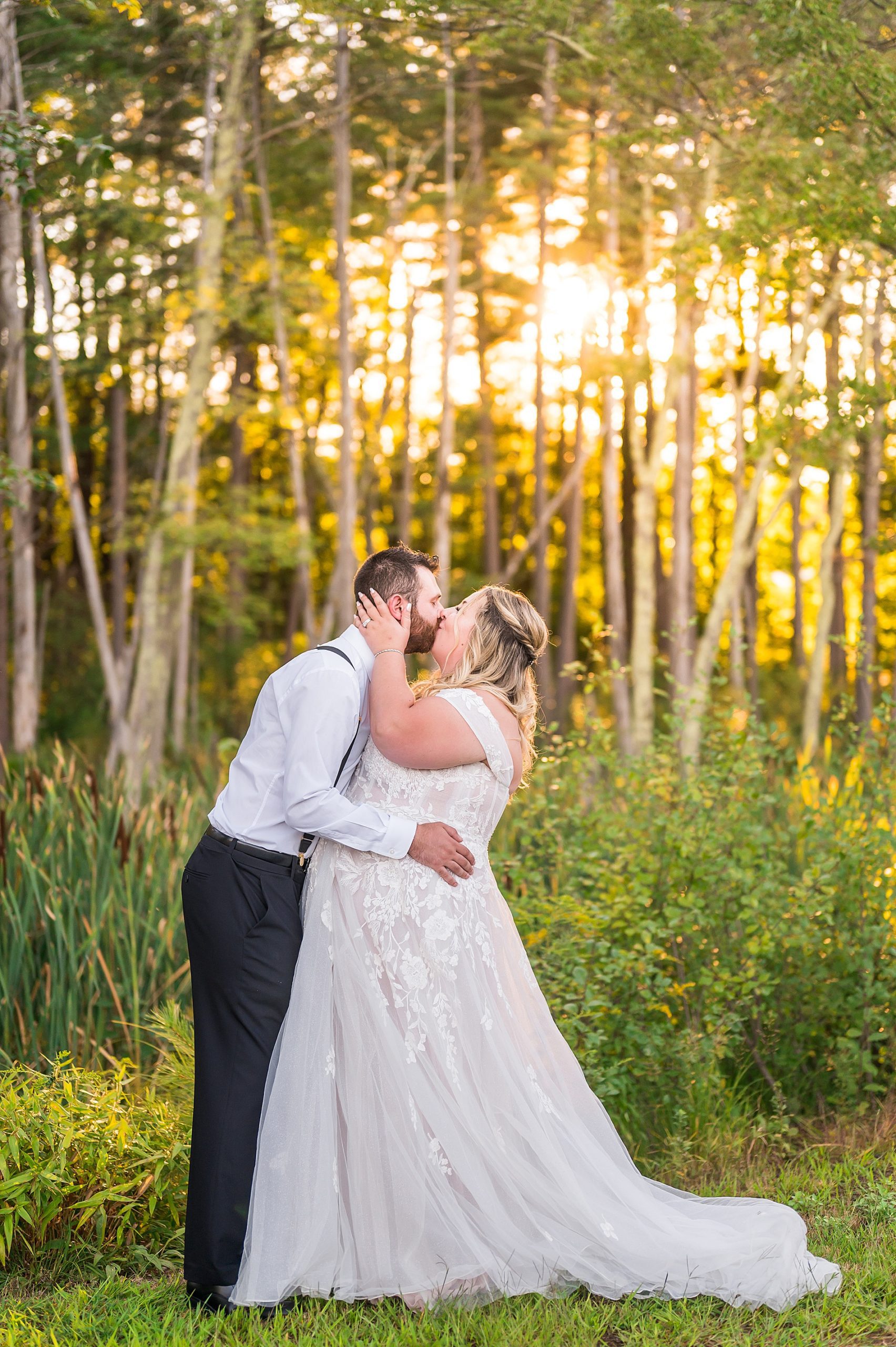 newlyweds kiss by woodline with sun streaming in the background