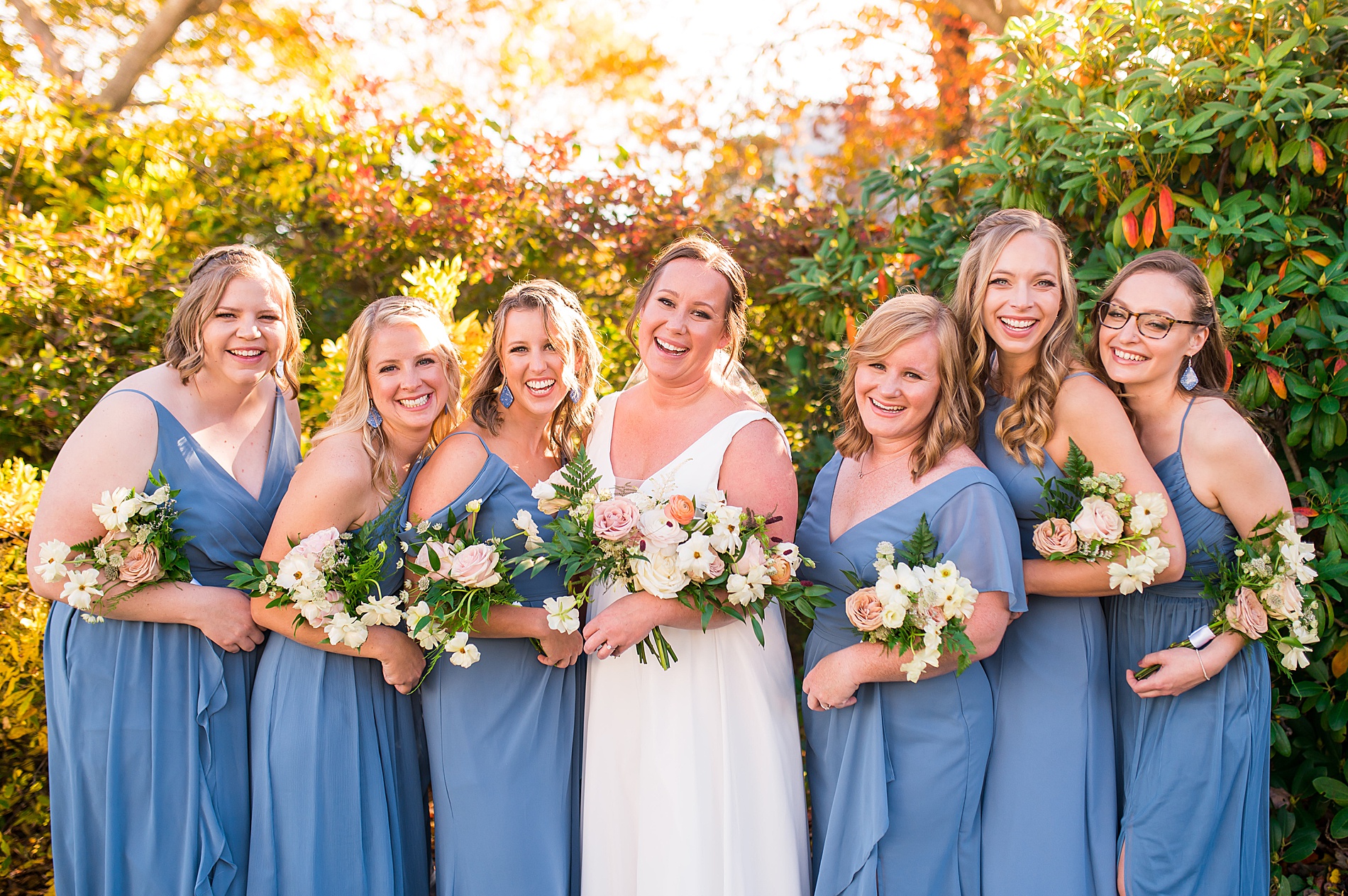 bridesmaids in steel blue dresses stand with bride holding wedding bouquets