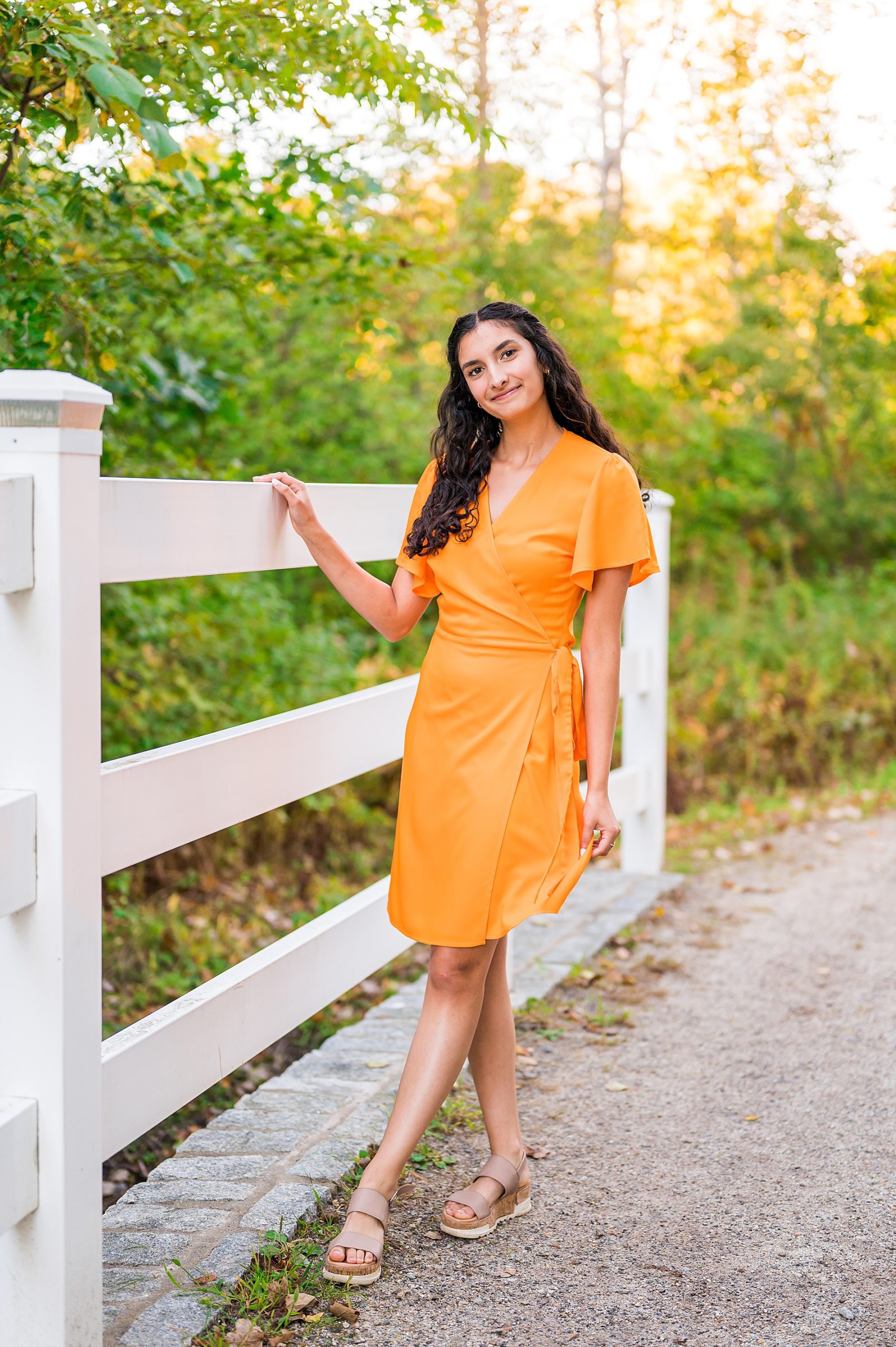 senior girl in yellow dress walks along white fence 
