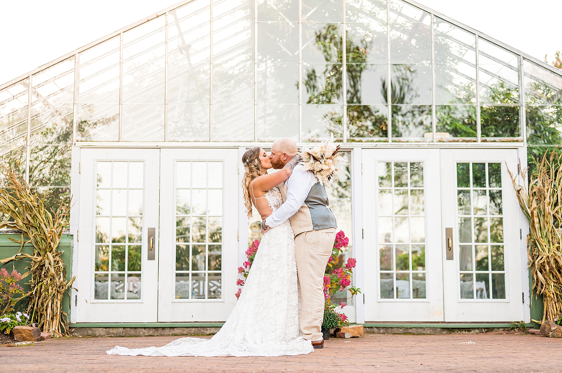 newlyweds kiss in front of greenhouse during wedding portraits 