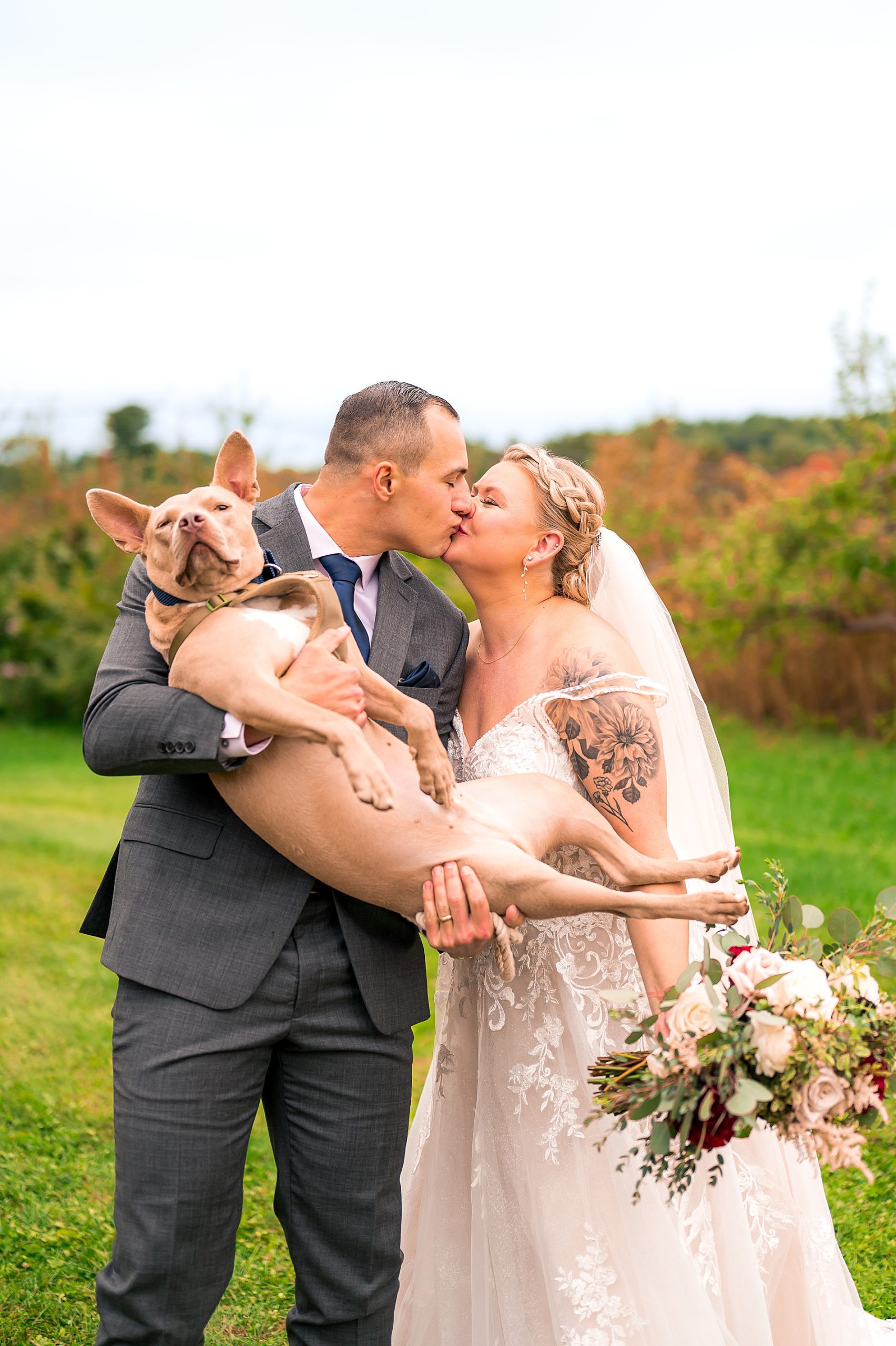 couple kiss as groom holds their dog in his arms