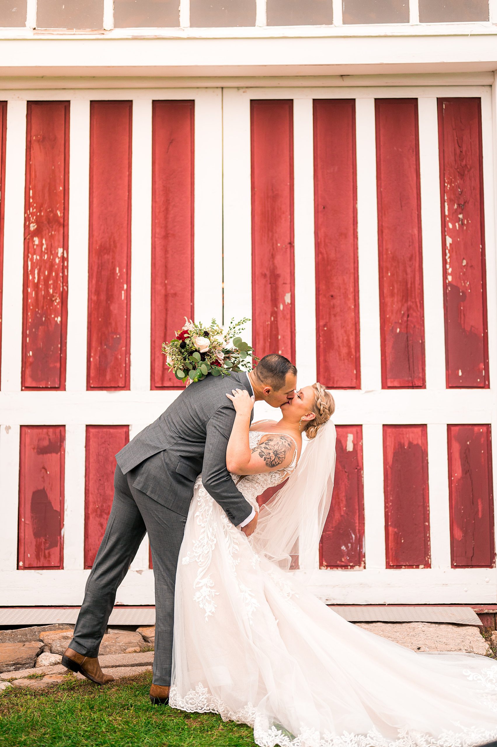 newlyweds kiss by white and red barn