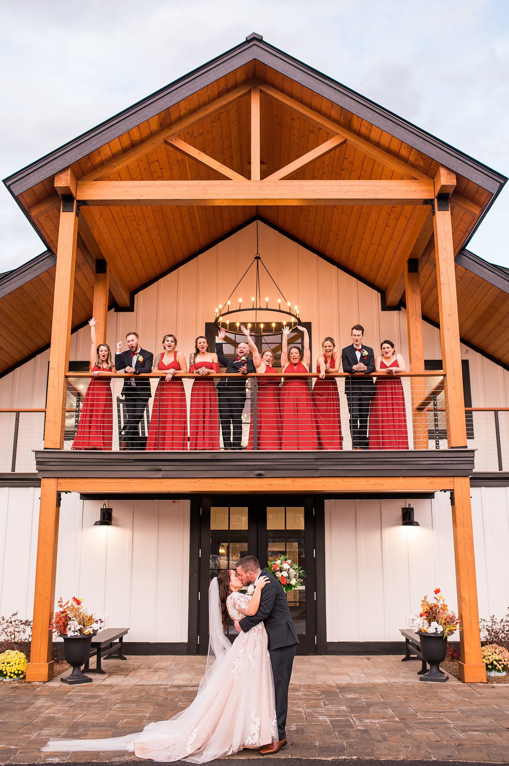 newlyweds kiss in front of The LakeHouse at Owl's Nest Resort while bridal party stands on balcony above