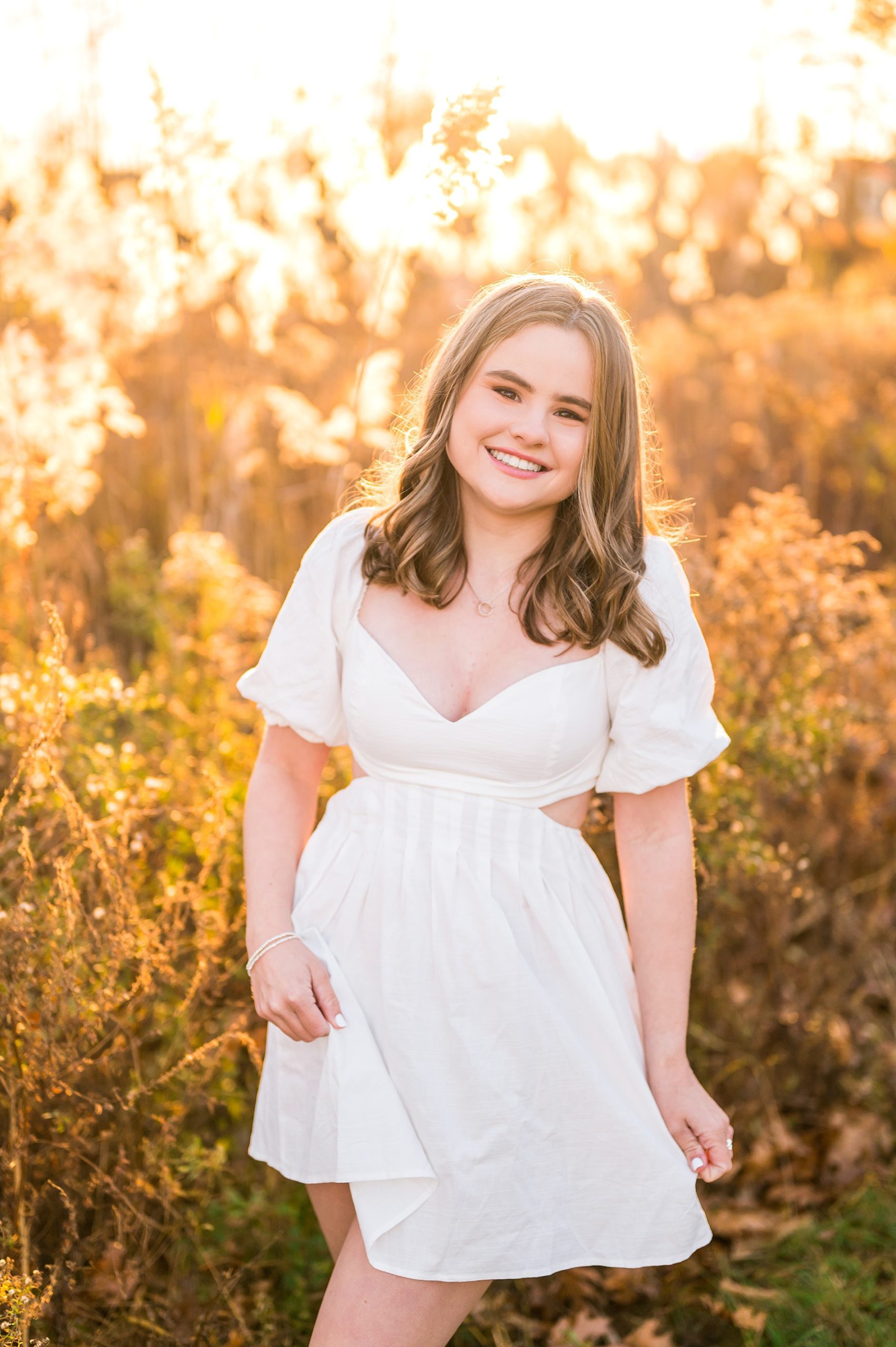 senior in white dress by field of tall grass