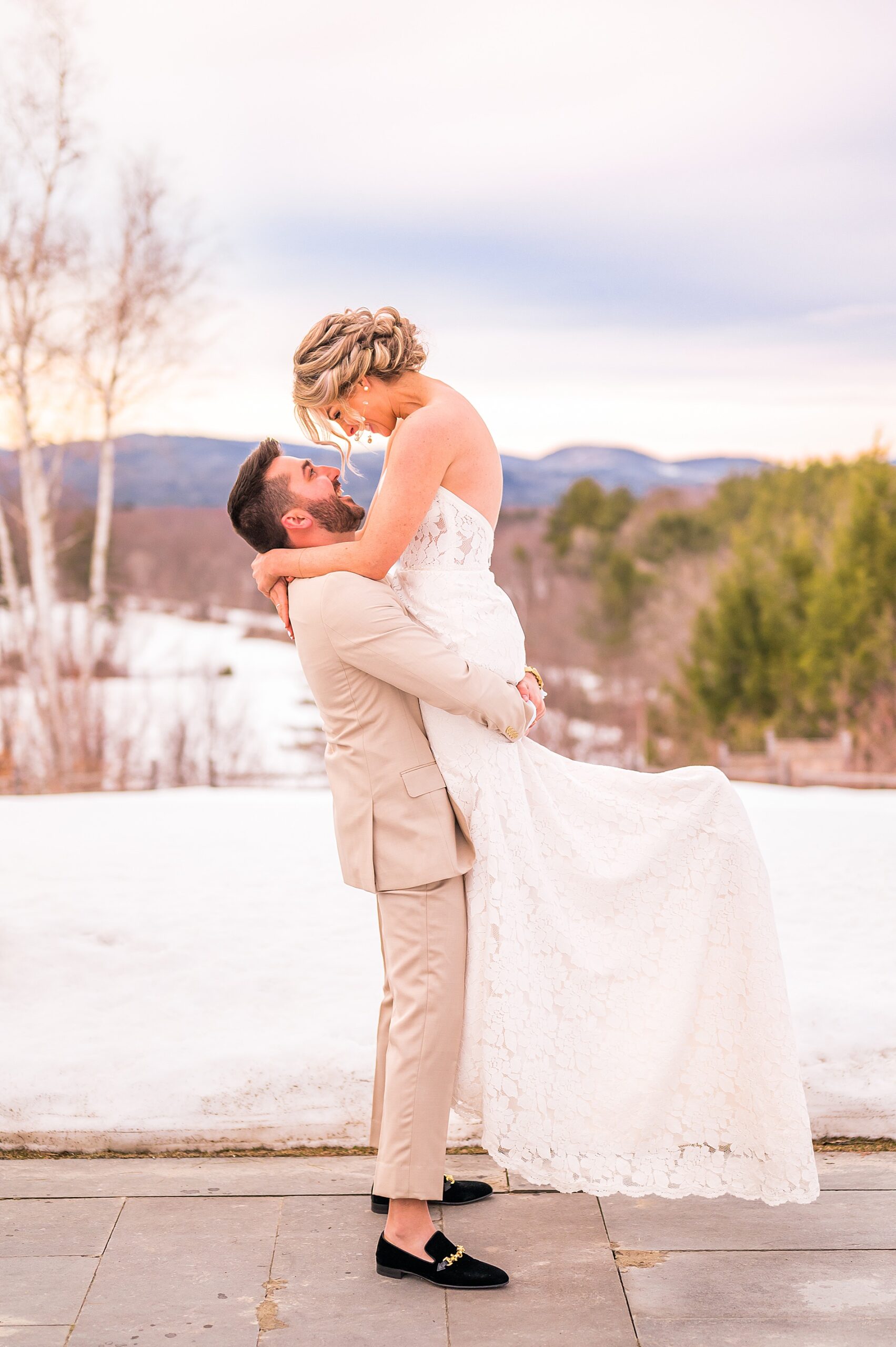 groom lifts his bride up with the mountains in the background