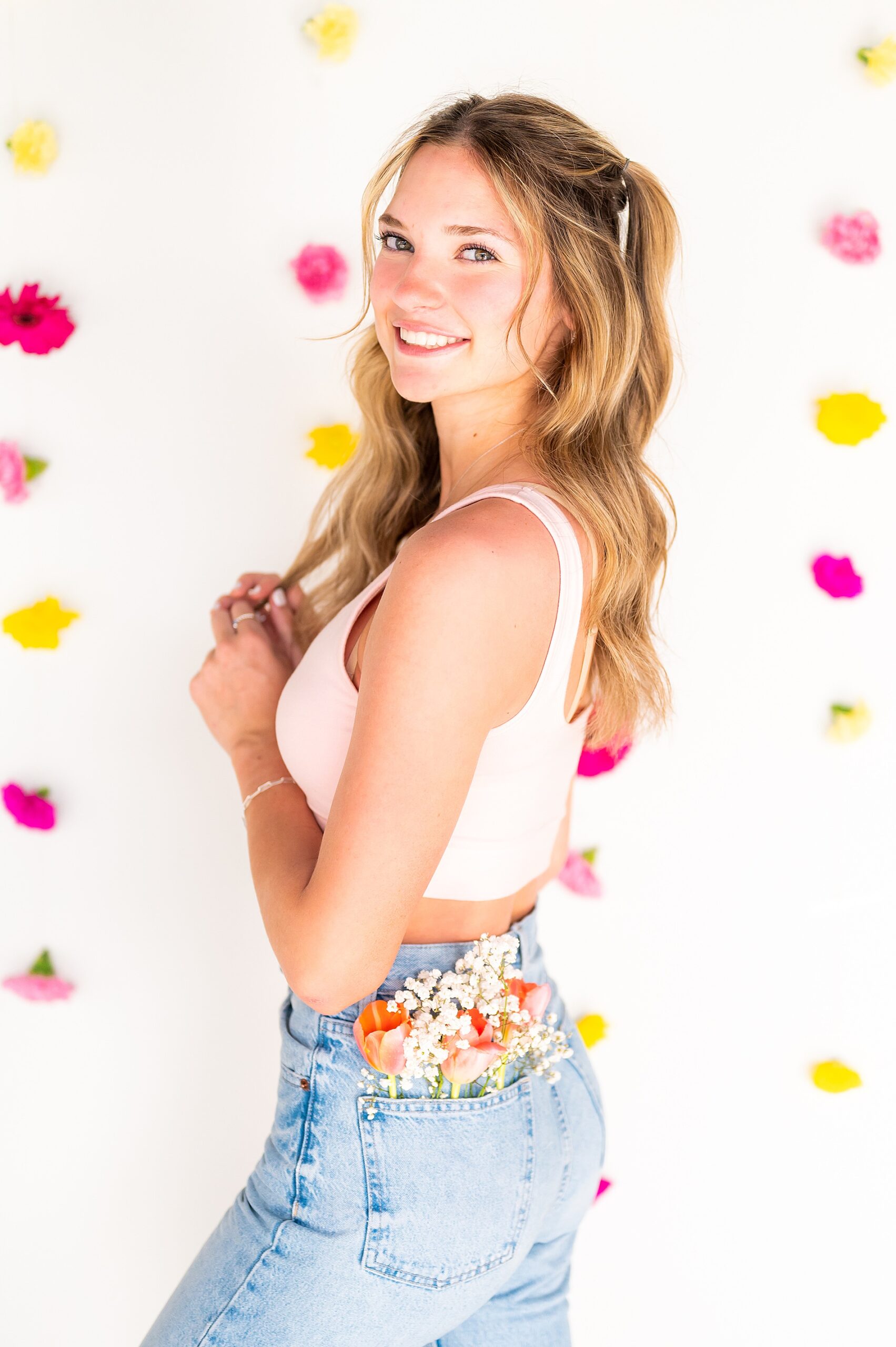 senior poses with flower backdrop and fresh flowers in her pocket 