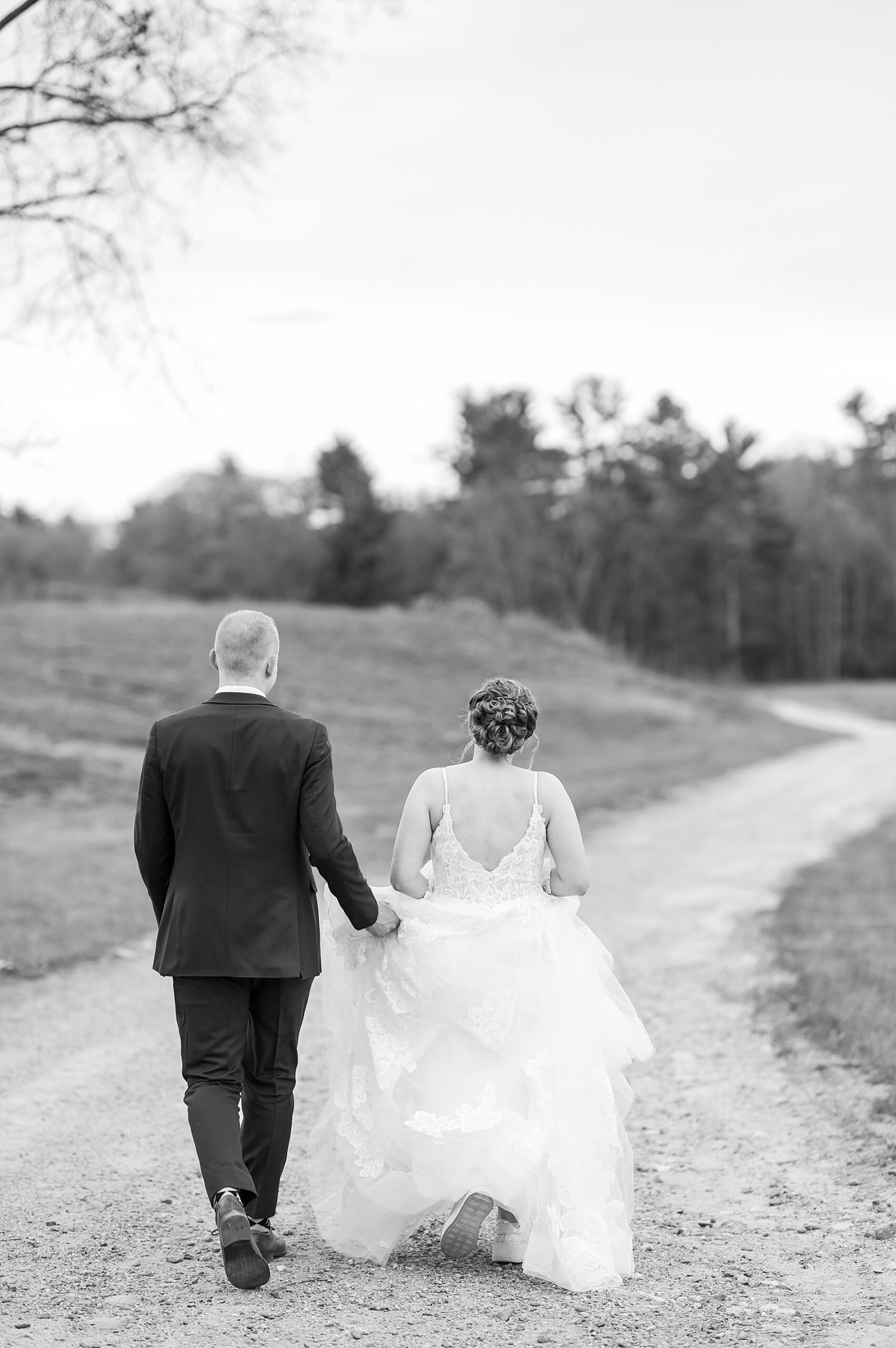 groom holds back of bride's dress as they walk together 