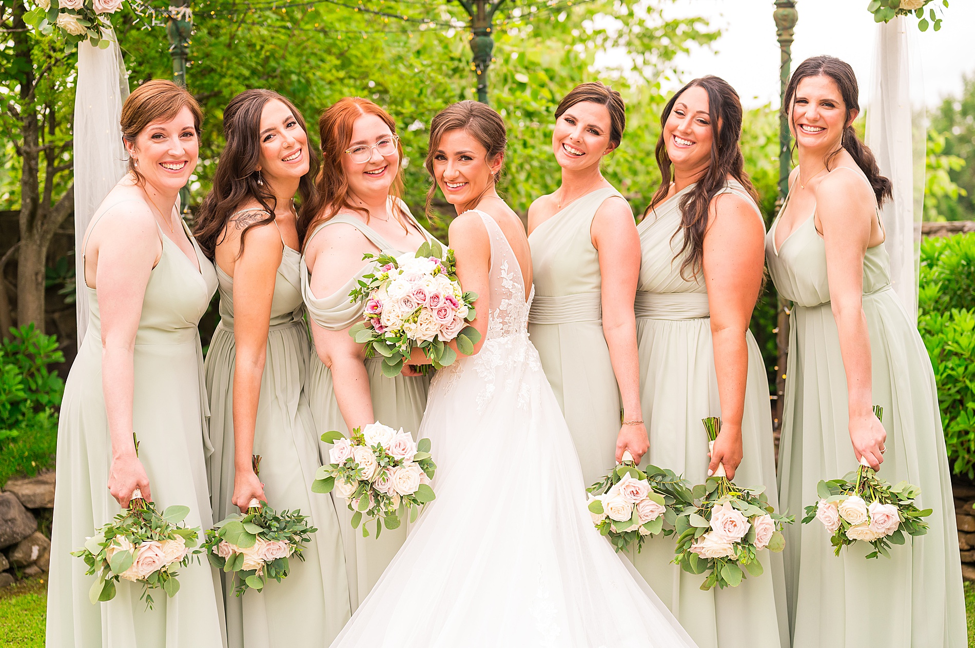 bridesmaids in sage green dresses with bride all holding white and pink summer bouquets  