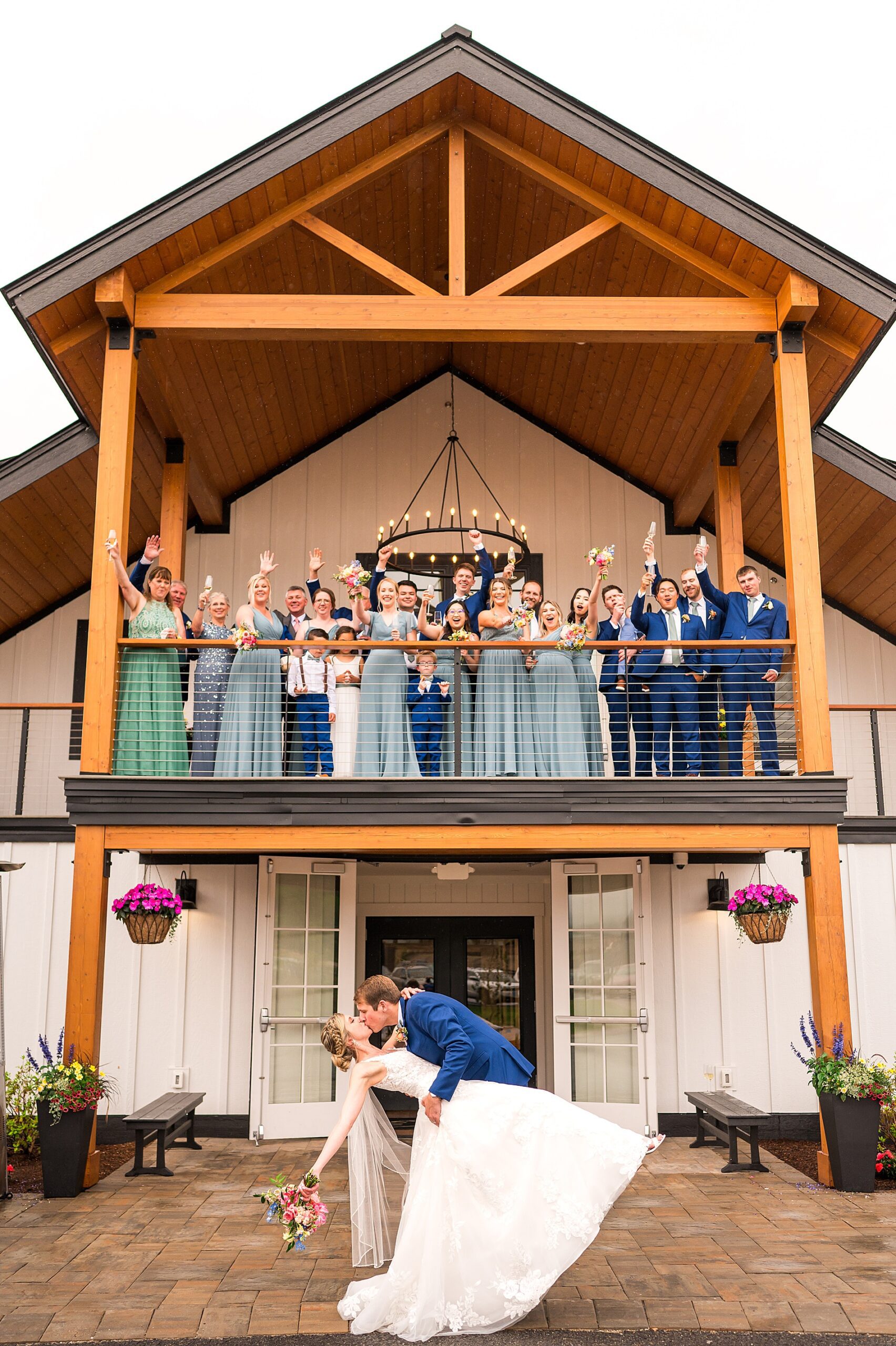 newlyweds kiss outside as wedding party cheers on balcony of lakehouse from  Summer Wedding at Owl's Nest Resort  