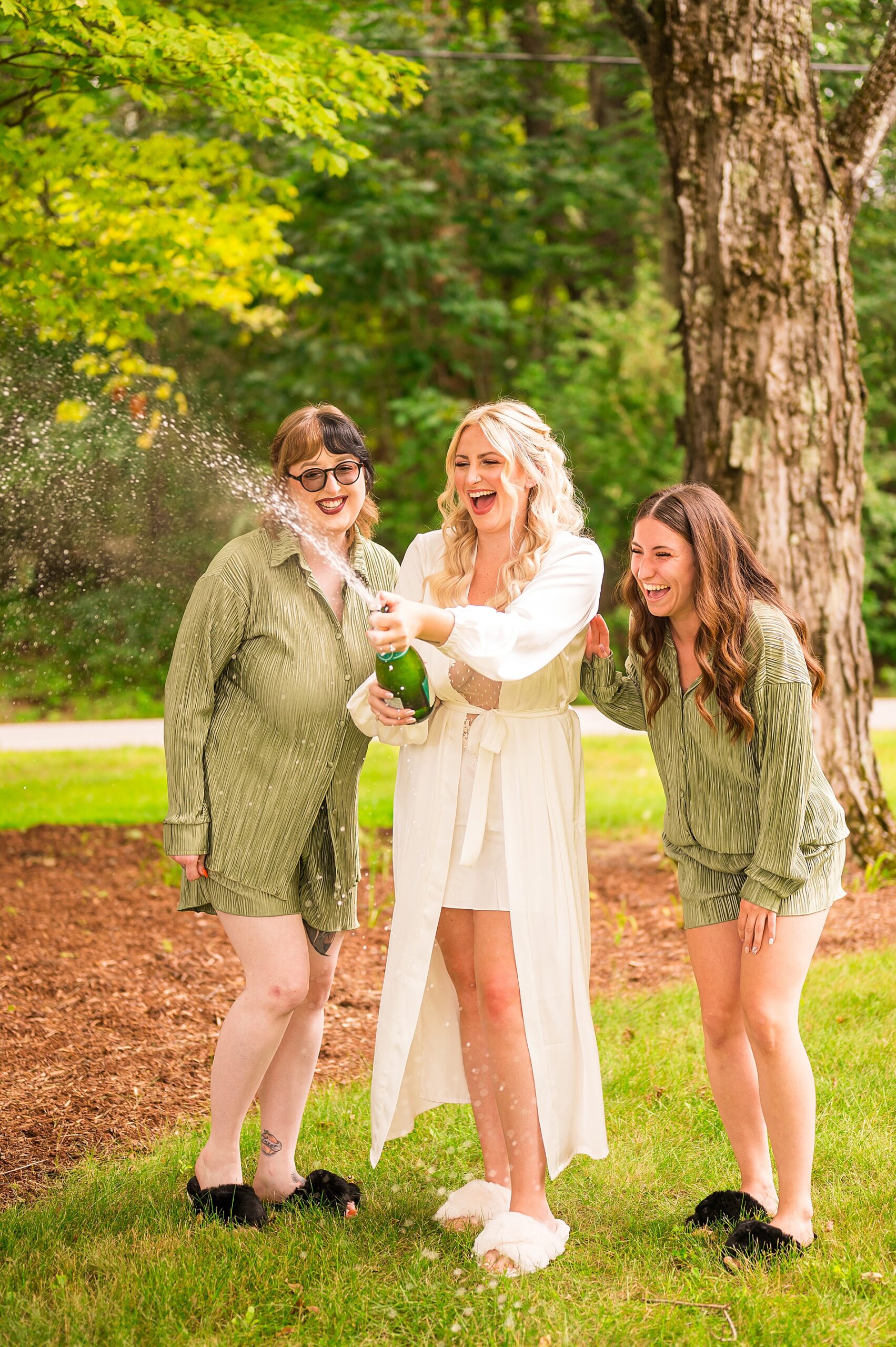 bride opening bottle of champagne with bridesmaids