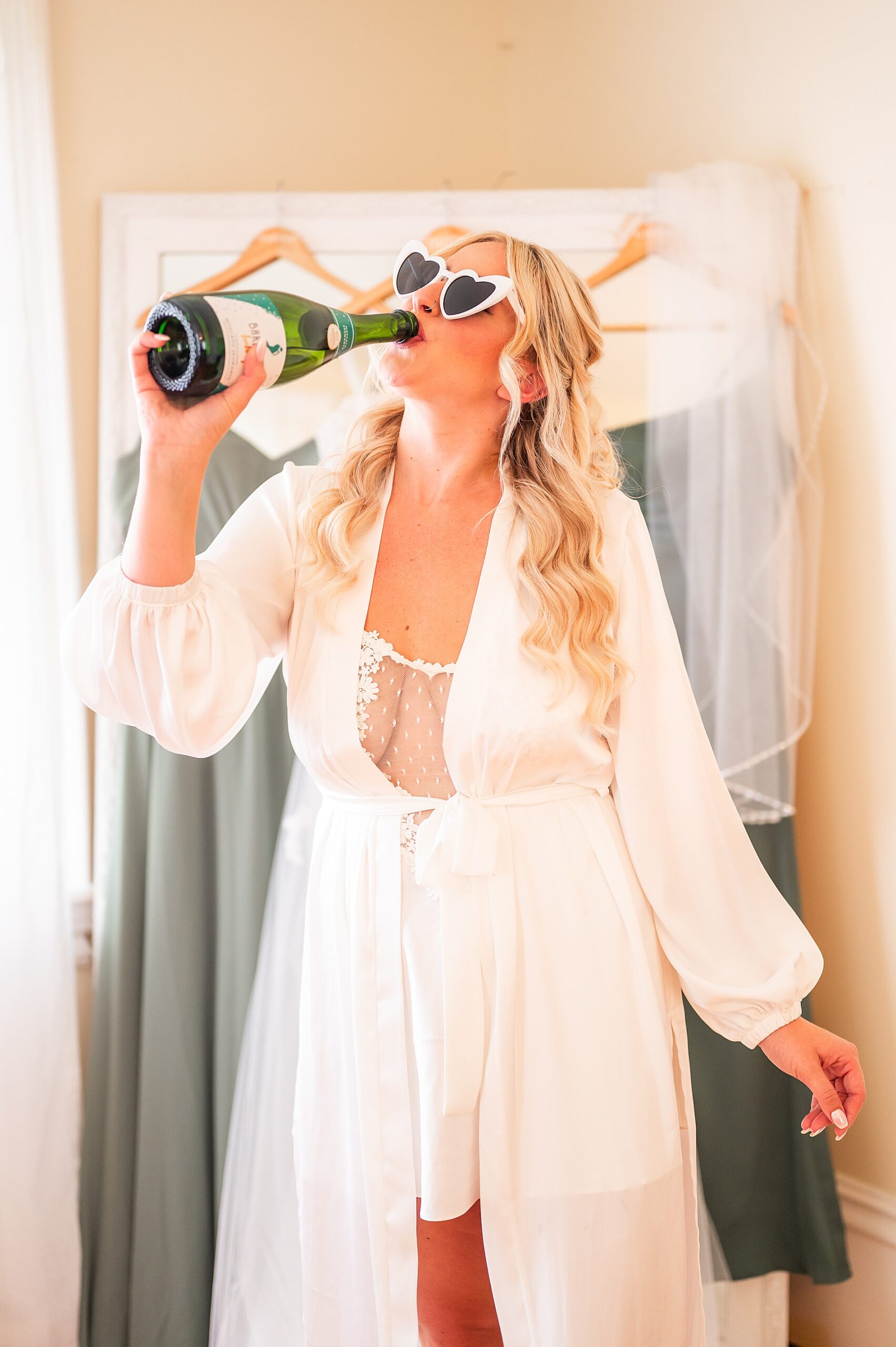 bride drinking champagne wearing white heart sunglasses