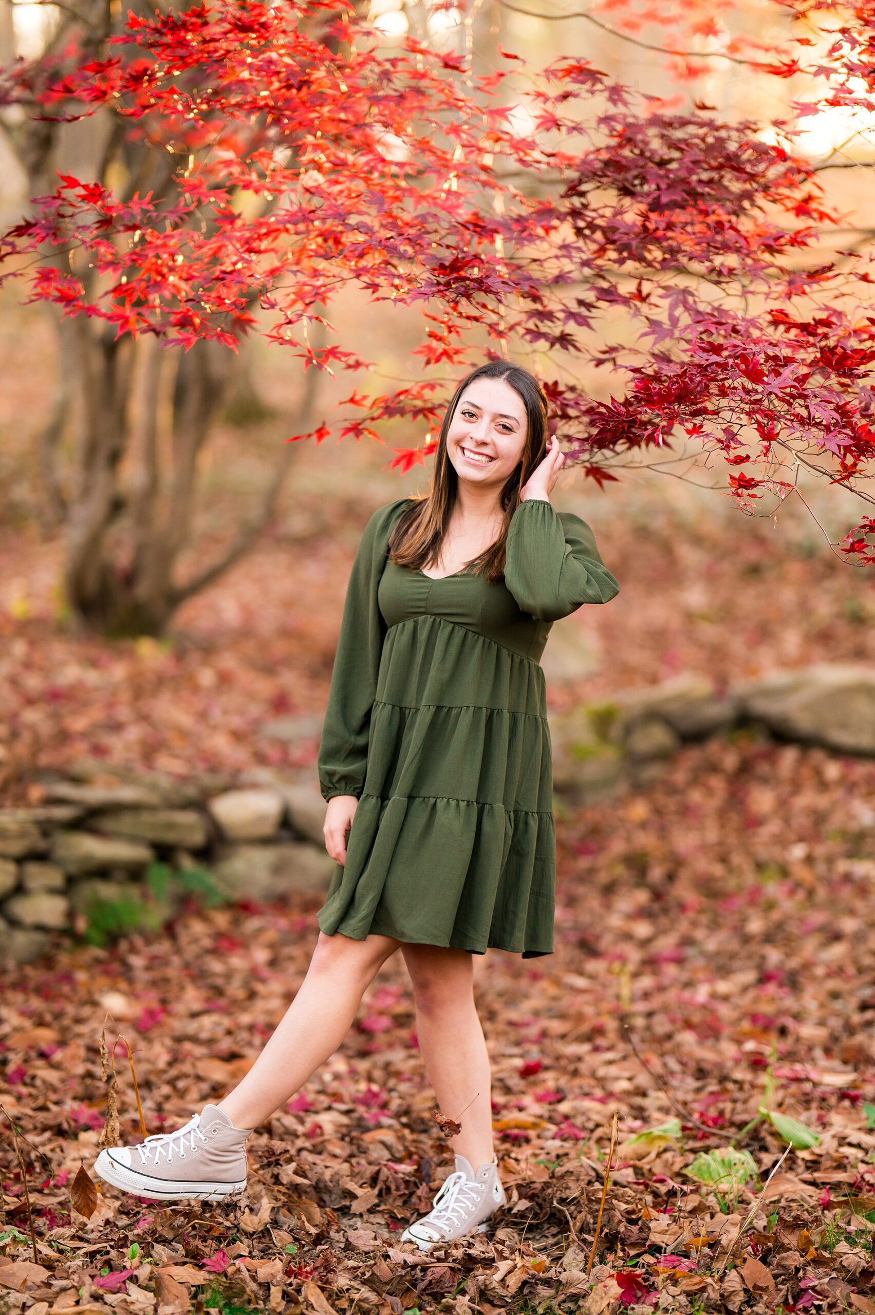 senior in olive green dress surrounded by maroon fall leaves
