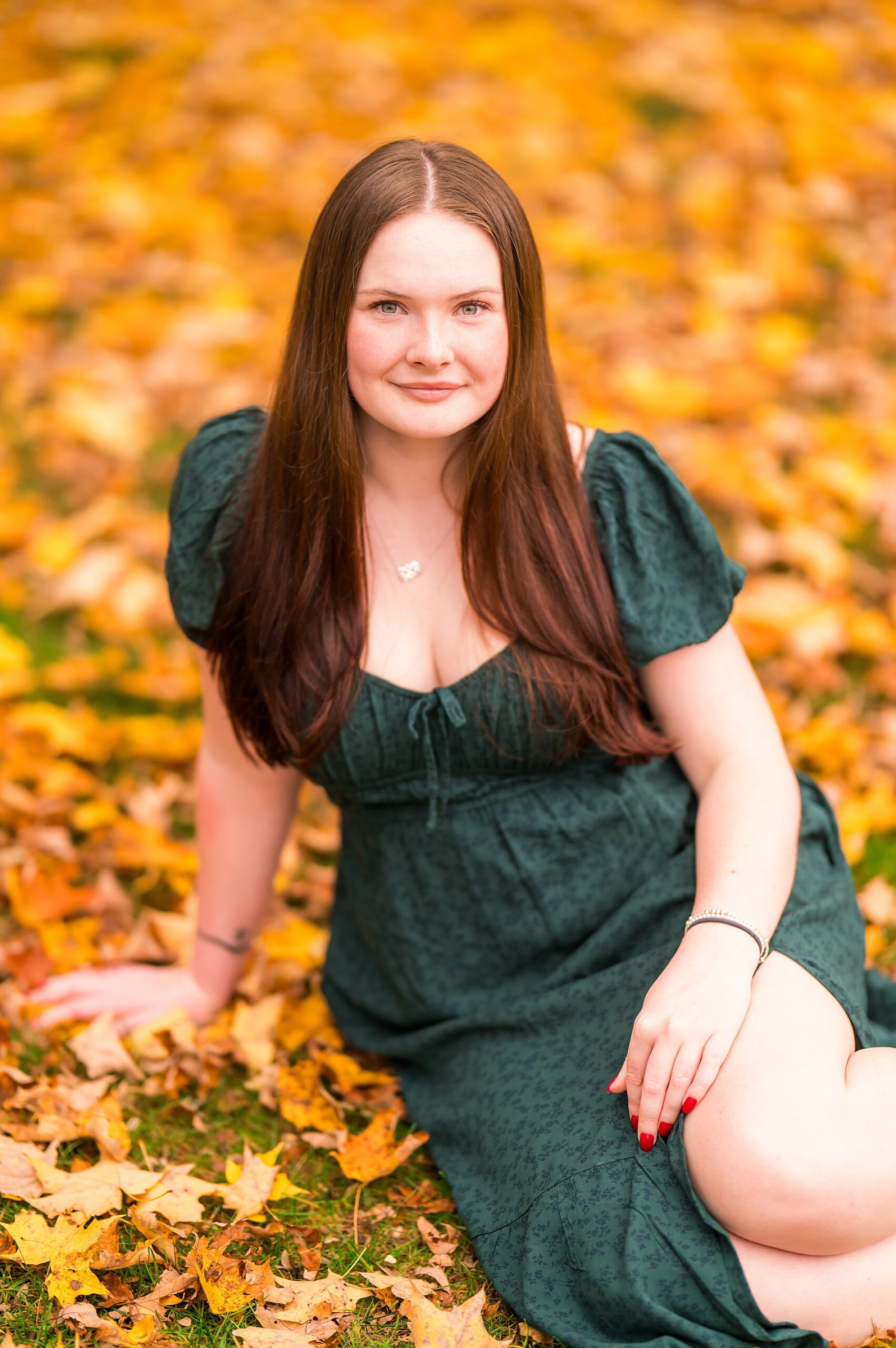 senior girl in jade dress sits in the fall leaves