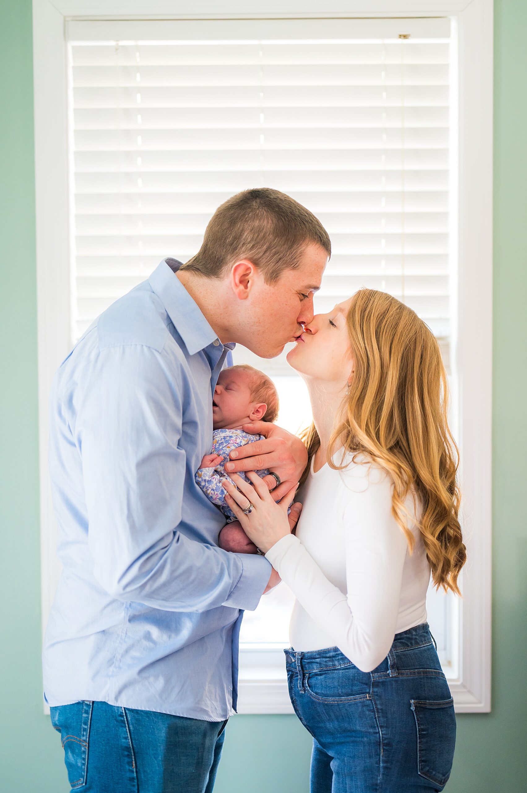 parents kiss while holding their newborn girl during In-Home Lifestyle Newborn Session 