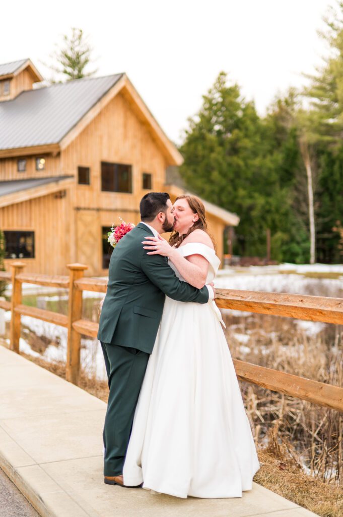 Bride and groom kissing in front of barn March wedding
